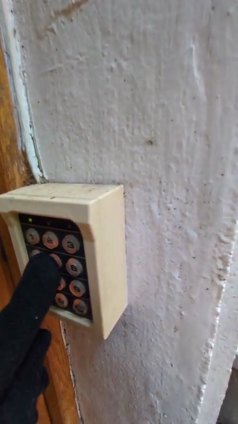 A gloved hand pressing a key on the Psych Ward Exit keypad, captured from the admin-only camera feed
